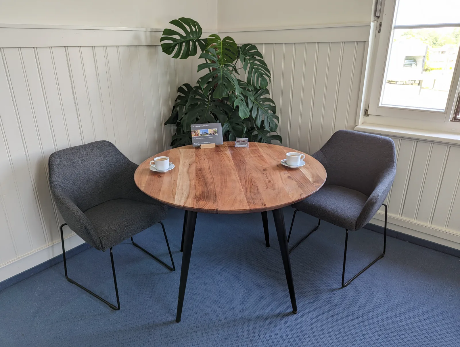 Besprechungsecke mit rundem Holztisch und zwei Sesseln im Büro von Pfyl's Treuhand