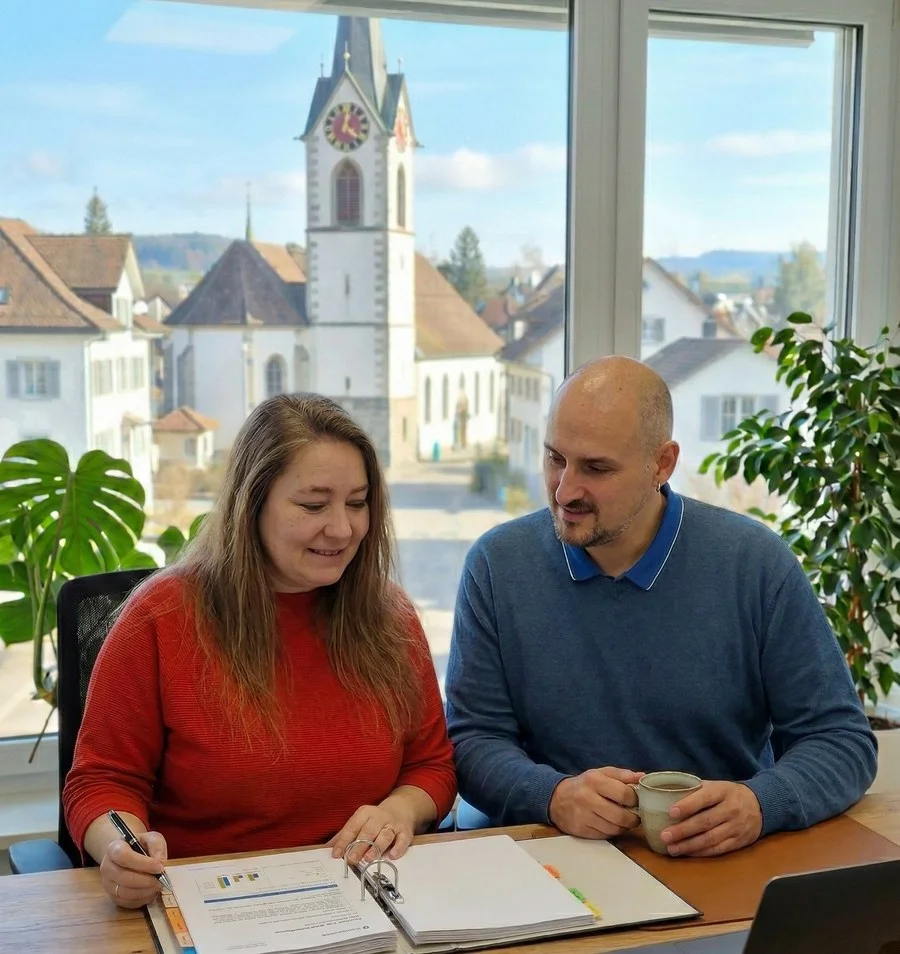Nicole und Samuel Pfyl besprechen Unterlagen im Büro, im Fenster die Kirche von Villmergen
